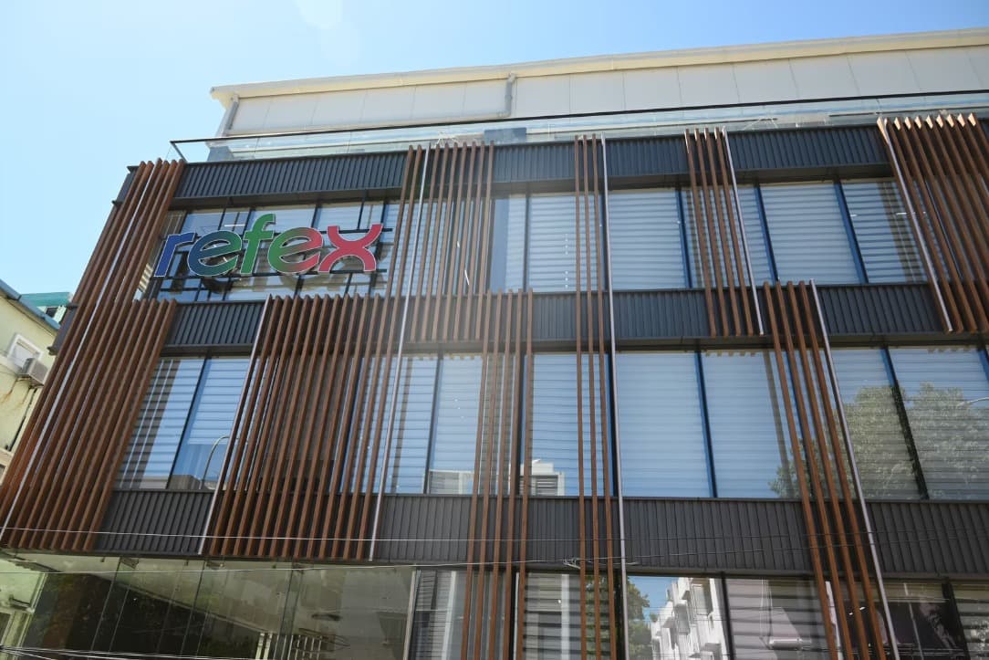 Large mural of a person with curly hair displayed on the exterior wall of the Refex Group building, featuring a modern balcony with wooden slats and surrounding greenery.